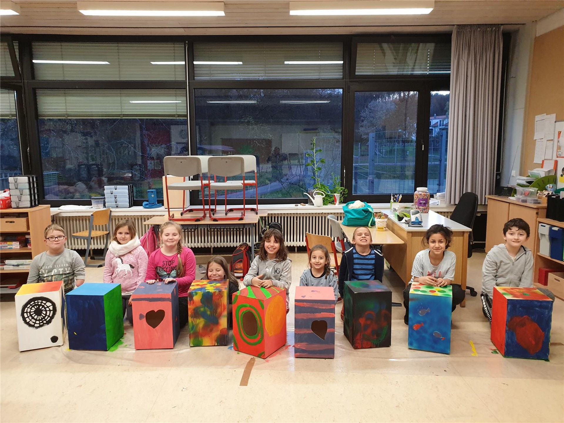 bunt bemalte Cajóns in einem KLassenzimmer mit den stolzen Schüler*innen im Hintergrund